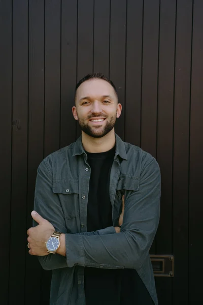 Kyle Hoffman smiling with arms crossed against a dark wood wall