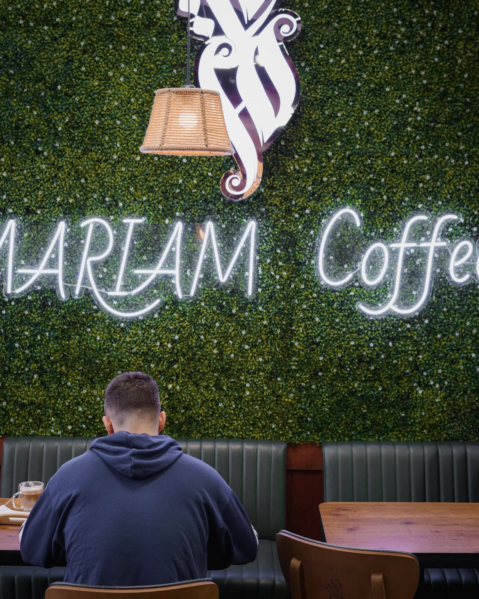Kyle Hoffman, seen from behind, seated beneath a neon coffee shop sign on a green wall