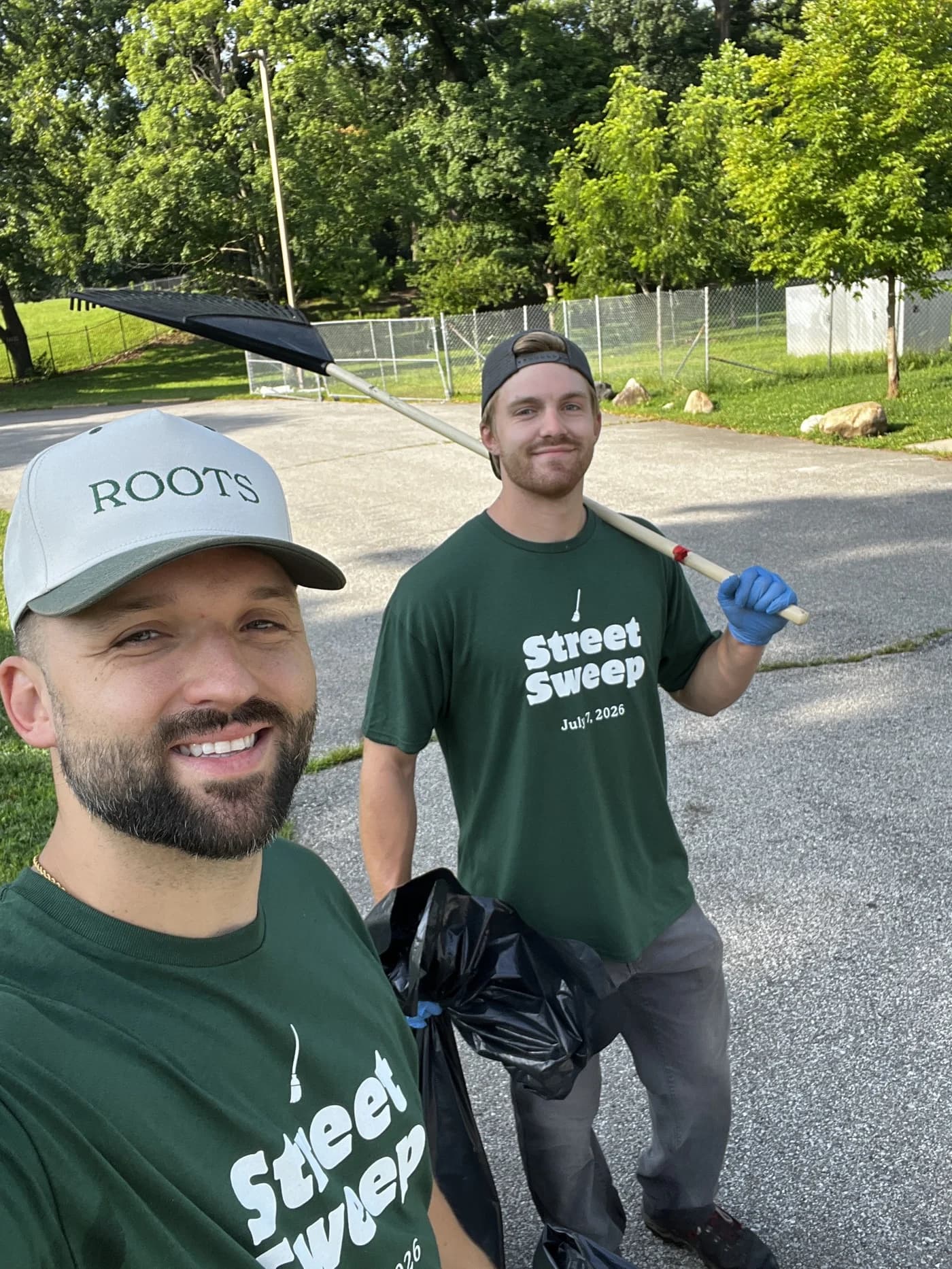 Kyle Hoffman in a Roots cap taking a selfie with a volunteer holding a rake, both in Street Sweep shirts