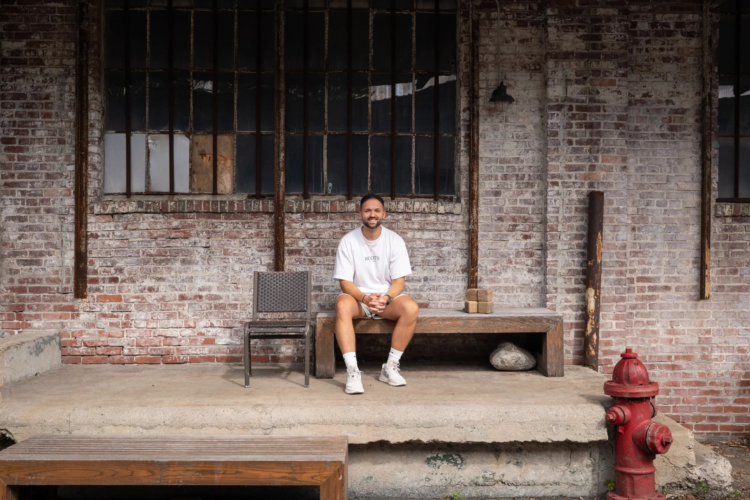 Kyle Hoffman smiling, seated on a wooden bench against a brick wall
