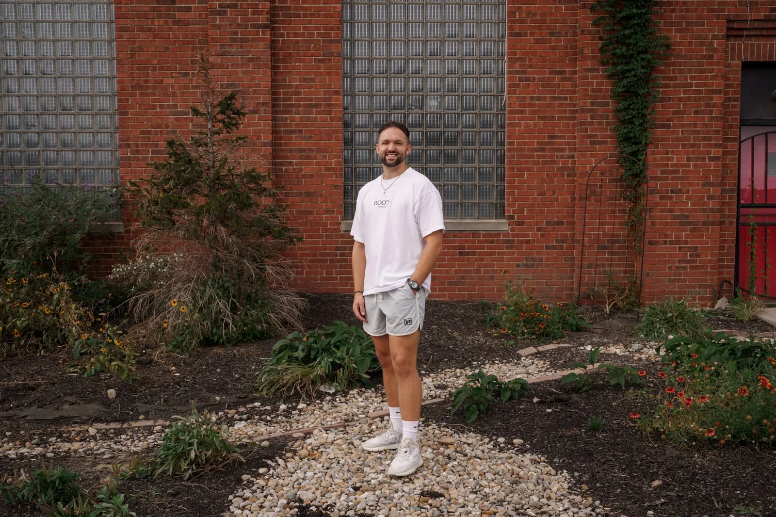 Kyle Hoffman smiling, standing beside a garden against a brick wall