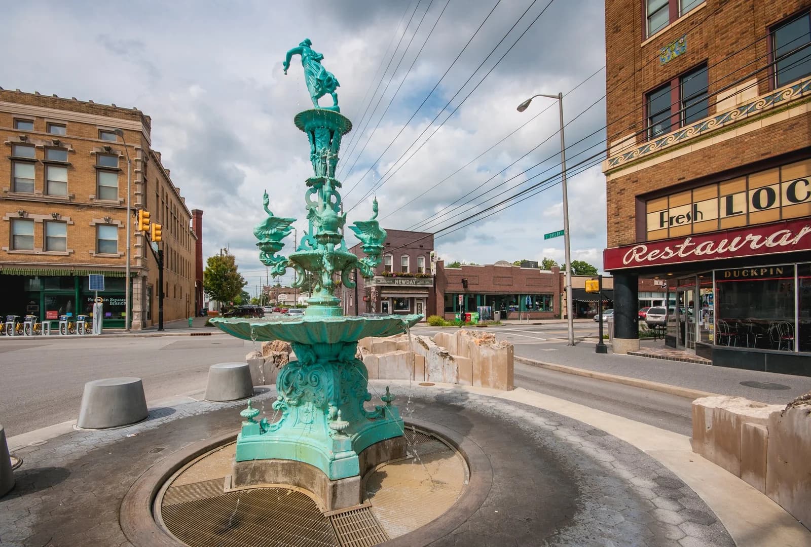 Green historic fountain at the intersection in Fountain Square, with brick storefronts and a restaurant sign